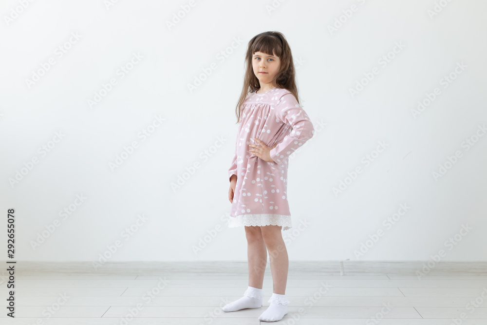 Little proud brunette girl in a pink dress is standing on a white background. The concept of stylish children's clothing and preschool age. Copyspace. Little proud brunette girl in a pink dress is standing on a white background. The concept of stylish children's clothing and preschool age. Copyspace.