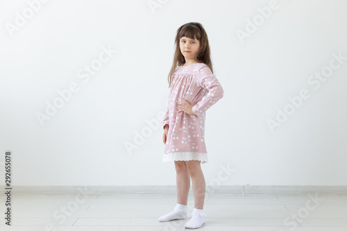 Little proud brunette girl in a pink dress is standing on a white background. The concept of stylish children's clothing and preschool age. Copyspace.