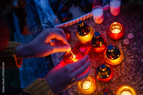 Woman light on red and yellow candles in the dark - to put them on a tombstone - all souls day preparing in the cemetery