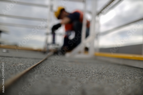 Defocused of rope access engineer inspector technician pull testing fall arrest, fall restraint roof anchor point horizontal safety line prior to used construction site Sydney, CBD, Australia © Kings Access