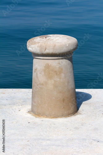 Newly made dark grey concrete mooring bollard looking like mushroom on top of concrete pier with calm clear blue sea in background on warm sunny summer day © hecos