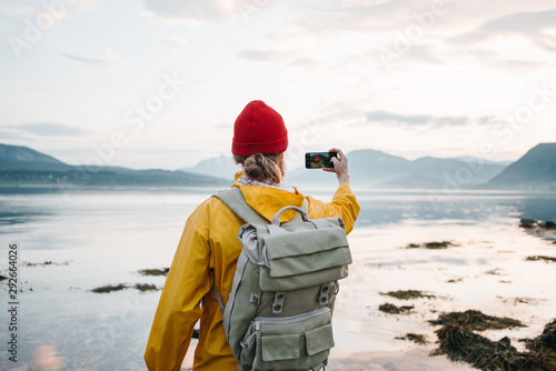 Traveler wearing yellow raincoat taking photo by smartphone fantastic nord landscape while traveling scandinavia. Man tourist takes a photo great mountain nature