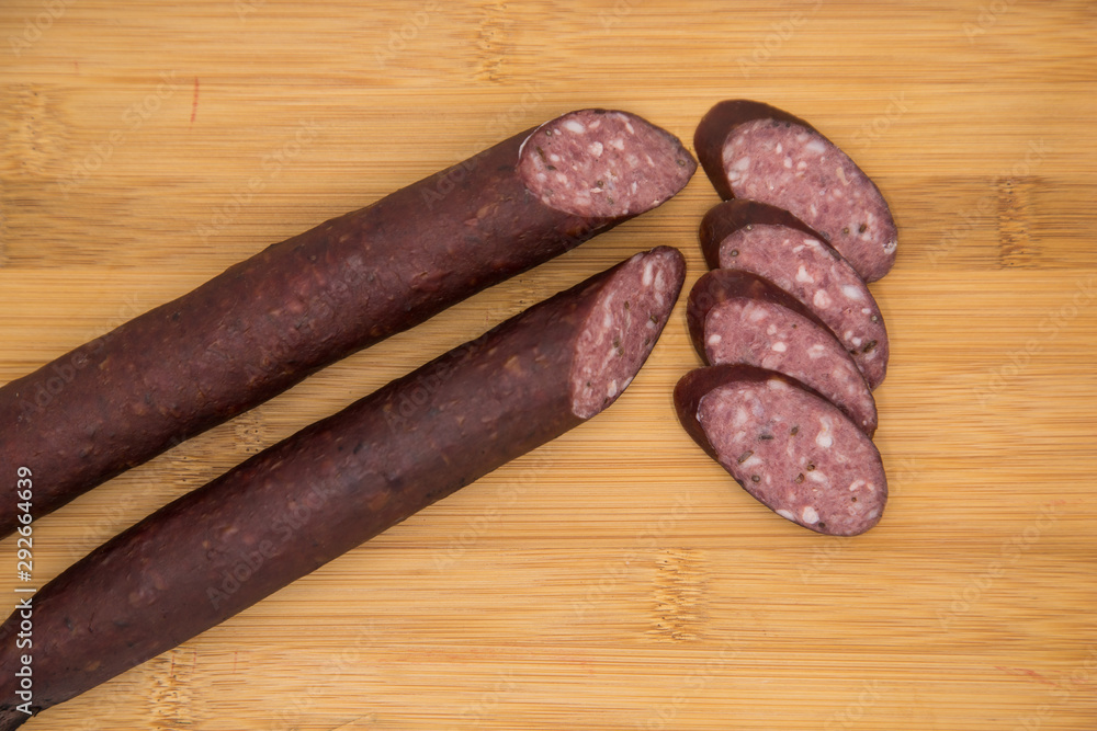 Two deer home sausages with thin slices on a wooden board. Wild meat delicacies for gourmets. Two deer home sausages with thin slices on a wooden board. Wild meat delicacies for gourmets.