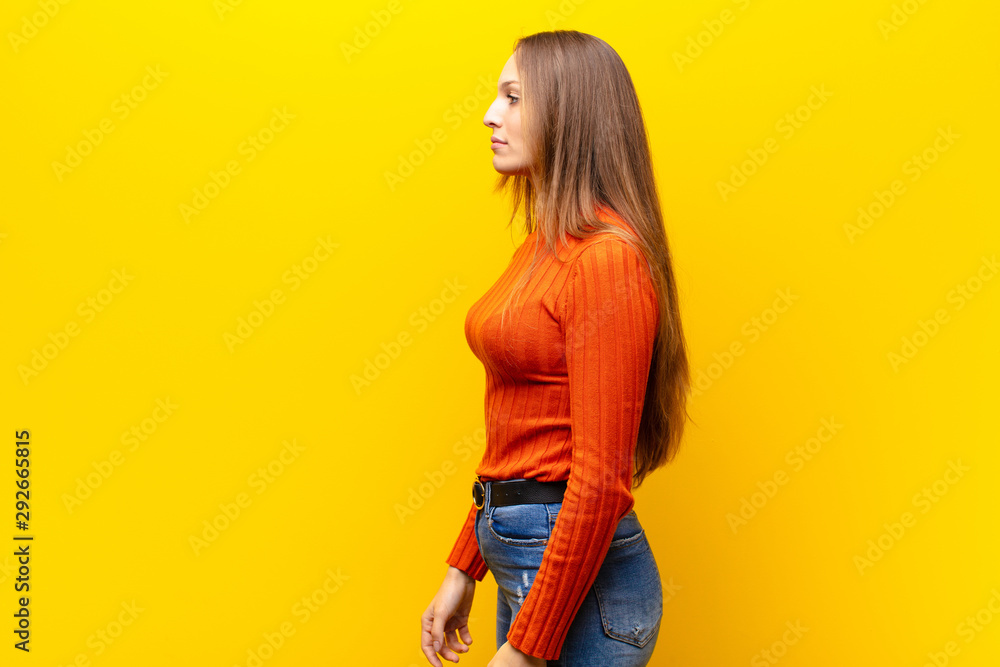 young pretty woman on profile view looking to copy space ahead, thinking, imagining or daydreaming against orange background - obrazy, fototapety, plakaty 