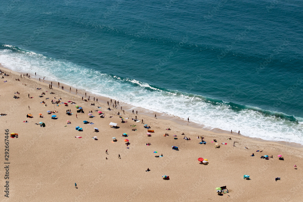 People on the beach  in front of Beautiful crushing wave of Atlantic ocean, captured during the walk along the sandy beach in Nazare, Portugal