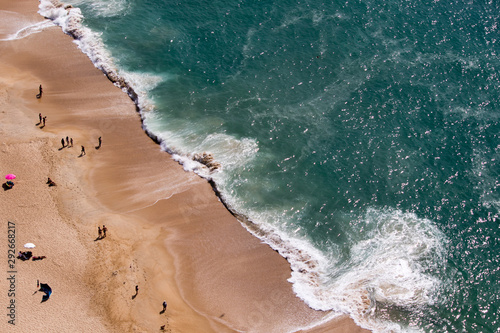 Drone view of people on the yellow sand beach facing the Beautiful crushing waves of Atlantic ocean in Nazare, Portugal