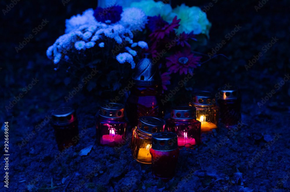 Candles in small lanterns on an earth grave - in the background flower  bouquets - all souls day decoration in a european christian cemetery - blue  hour outdoor shot Stock Photo | Adobe Stock