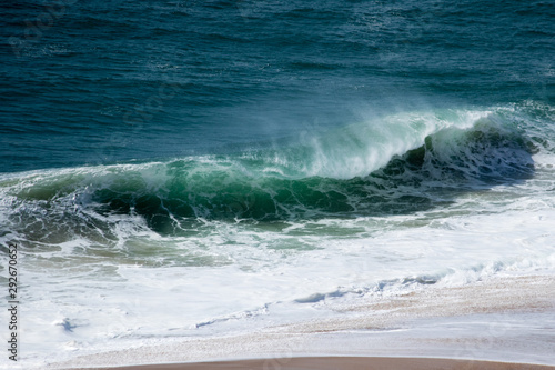 Beautiful crushing wave of Atlantic ocean, captured during the walk along the sandy beach in Nazare, Portugal