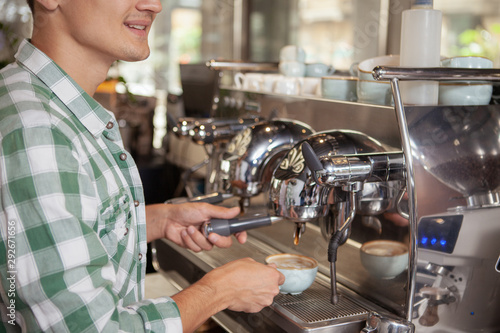 Cropped shot of a cheerful male barista smiling  using coffee machine  preparing drink for a customer