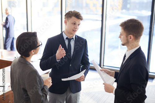 Group of young business people gesturing actively while standing in conference room and discussing project ideas, copy space