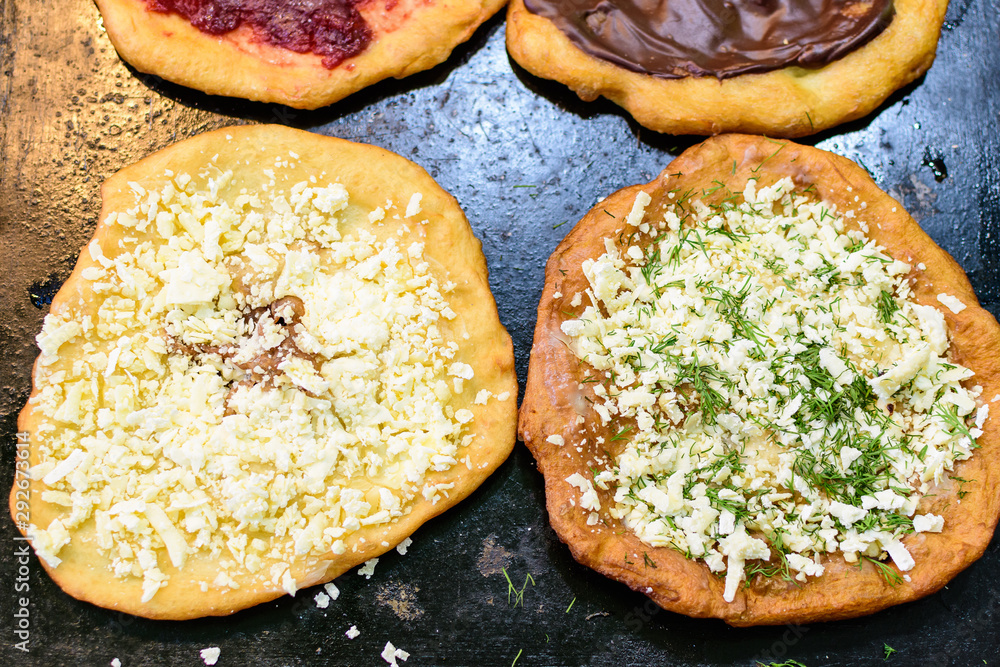 Close up of a langos, typical Hungarian food specialty, with white cheese and dill on an iron sheet, deep fried dough in direct sunlight, available for sale at a street food market 