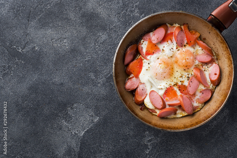 Pan with fried eggs sausages and tomatoes on the table. Rich homemade Breakfast.