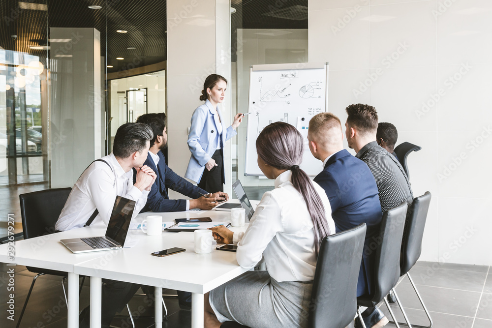 Company leader standing near the flipchart. A team of young businessmen working and communicating together in an office. Corporate businessteam and manager in a meeting