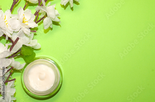 Beautiful composition with cosmetics on light green background  flat lay with skin cream and wthite flowers  spring background with a copy space for an your text  clean beauty concept  top view