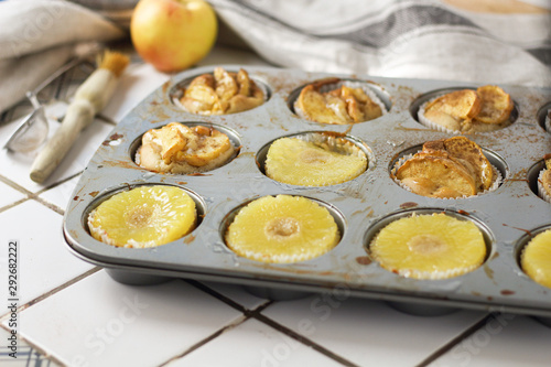 Muffins cupcakes with pineapple circles and apple slices in a cupcake muffin tray, on kitchen white tile near with pastry brush. Cake dessert photo for cook book recipe top view