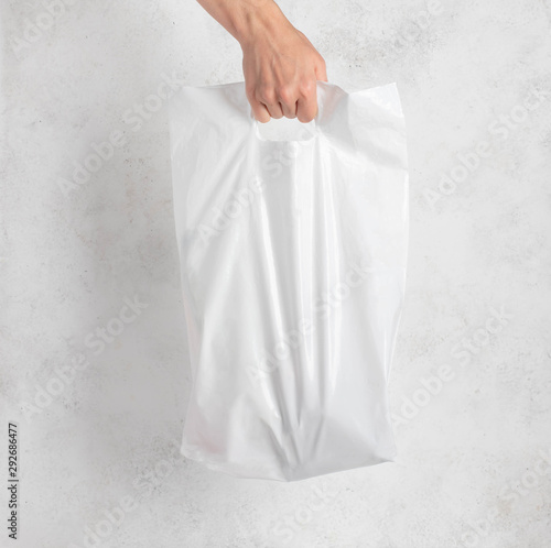 white plastic bag held by a woman's hand. light background.