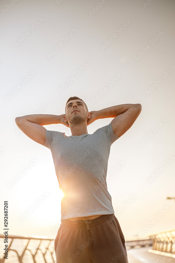 Strong good-looking young man is stretching outdoors Strong good-looking young man is stretching outdoors