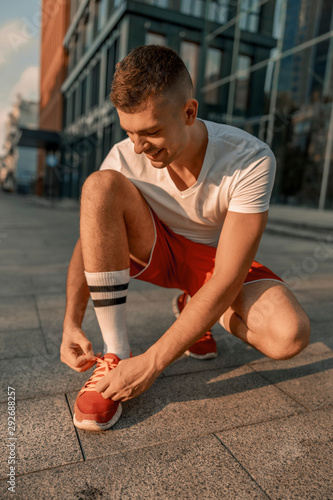 Contented young sportsman tying a shoelace outdoors