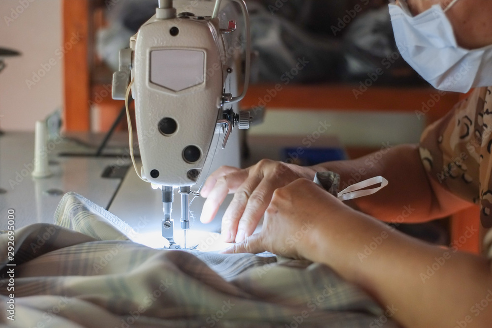 Hand of the seamstress is using a white industrial sewing machine to sew cloth.