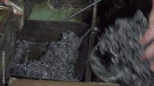 working engineer in the factory, removes metal shavings with his hands from the compartment into the trash.