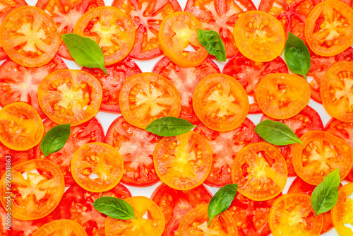 trendy pattern of sliced ripe red, yellow and orange tomatoes decorated green leaves of basil on white background, flat lay