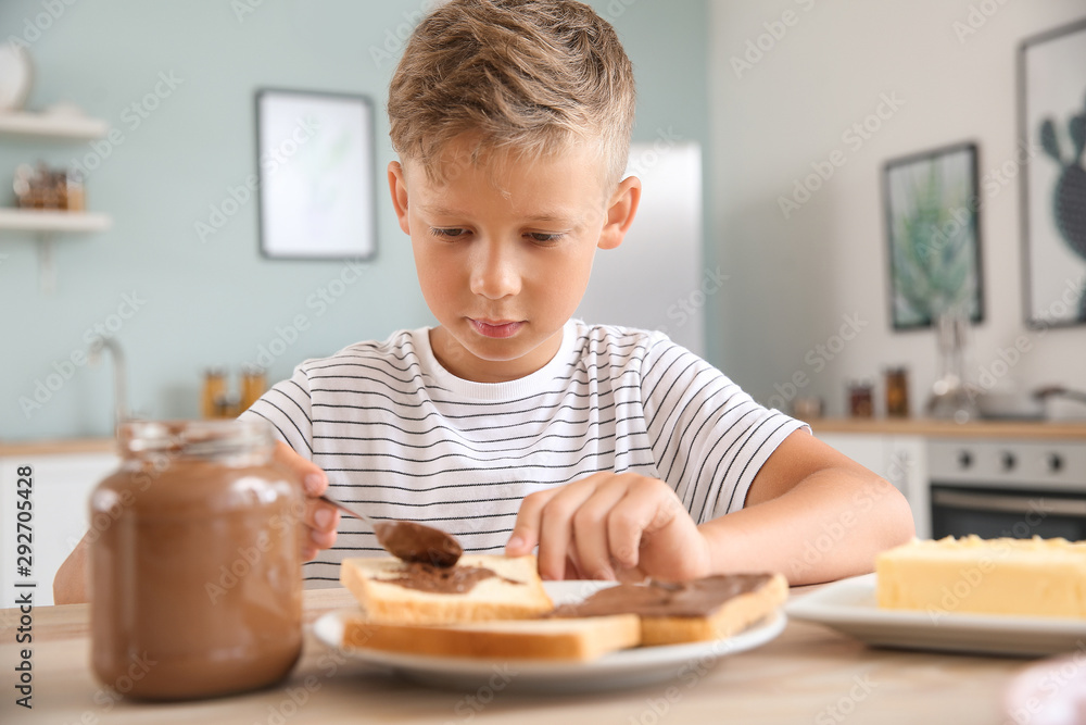 Funny little boy eating tasty toasts with chocolate spreading in kitchen Funny little boy eating tasty toasts with chocolate spreading in kitchen