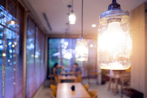 Light bulb hanging in restaurant with dating couple blurred in background. Dinner table in cafe background with shiny light.