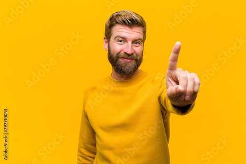 Tableau sur toile young blonde man smiling and looking friendly, showing number one or first with