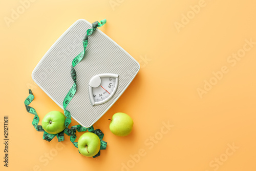 Fotografie Scales, apples and measuring tape on color background