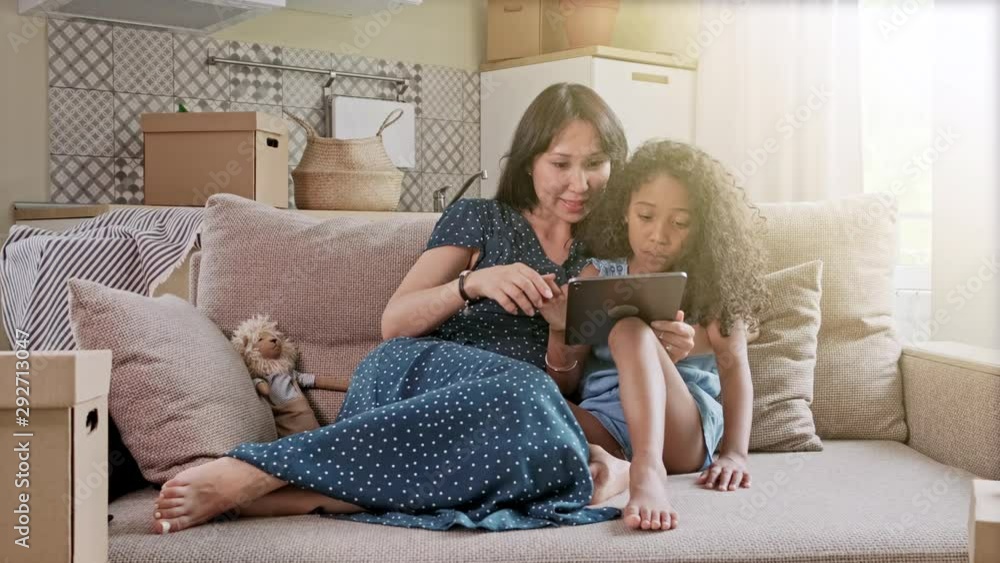 Mother and Daughter having fun on a digital tablet in a home interior. A cute happy mother and daughter using a digital tablet at home in the living room.