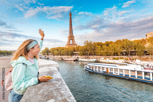 Photography A girl tourist in a hat standing on a bridge and waving to a river cruise sailin