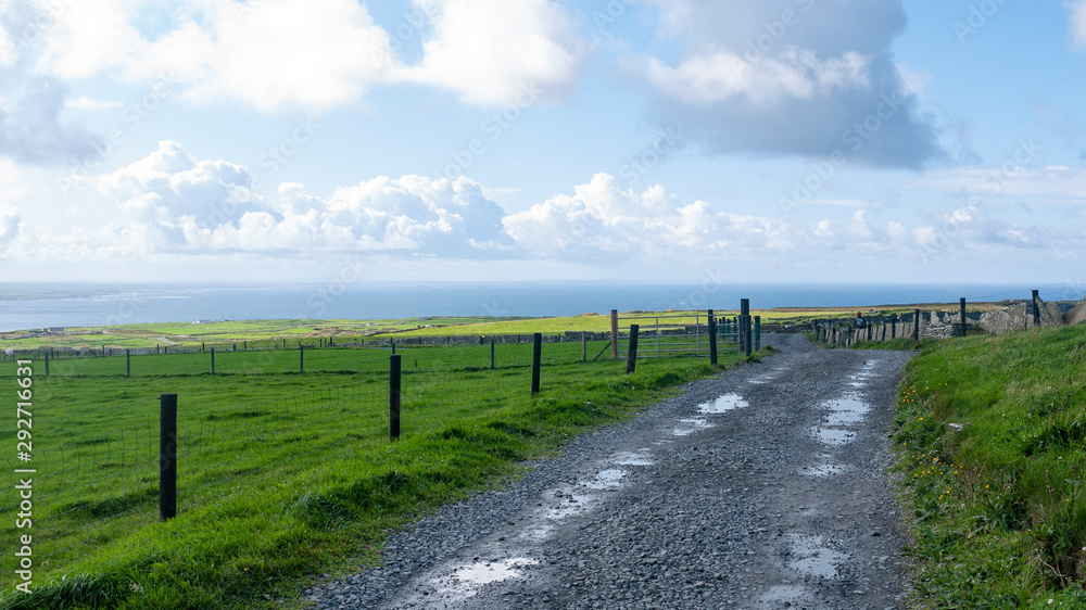 Dirt road through agricultural grassy fields, taken in County Clare, Ireland showing the ocean in the background taken in summer.