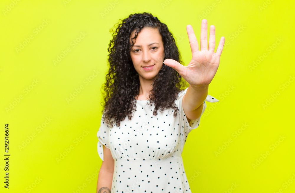 young pretty woman smiling and looking friendly, showing number five or fifth with hand forward, counting down against chroma key wall - obrazy, fototapety, plakaty 
