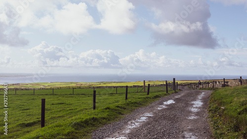 Dirt road through agricultural grassy fields  taken in County Clare  Ireland showing the ocean in the background taken in summer.