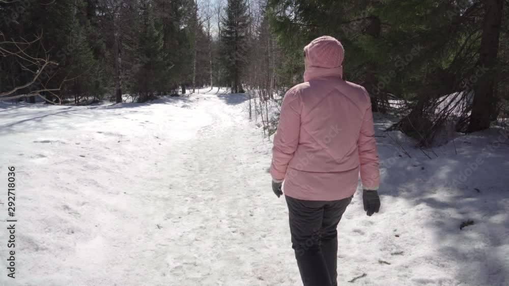 Grandma walks briskly in a pink jacket through the winter forest. Aged woman. enjoys life and nature in a good mood