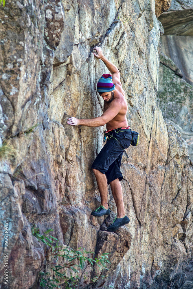 Side view of a young climber hanging on a rock, free space.