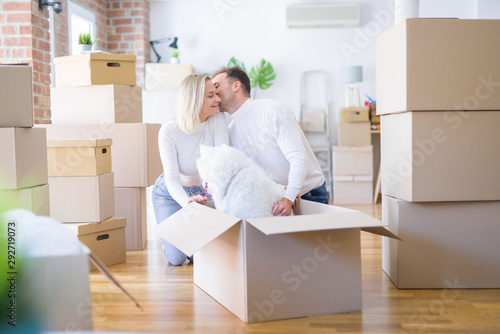 Young beautiful couple with dog kissing sitting on the floor at new home around cardboard boxes