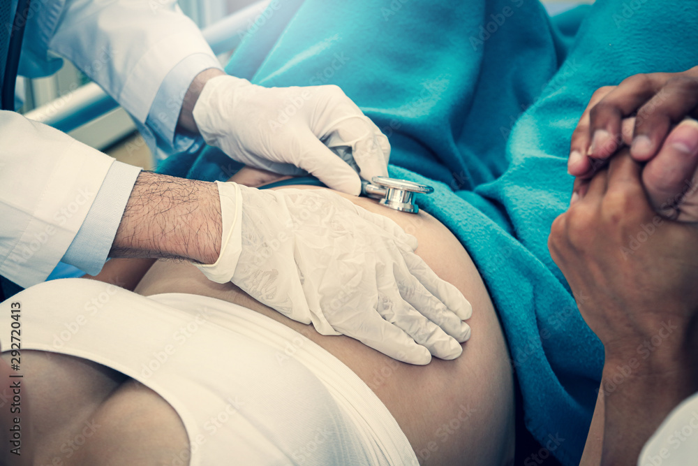 The doctor wears white gloves using a stethoscope to check the pregnancy of the girl. Husband shook hands with his wife to encourage