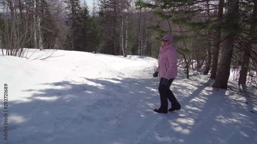 Grandma walks briskly in a pink jacket through the winter forest. Aged woman. enjoys life and nature in a good mood