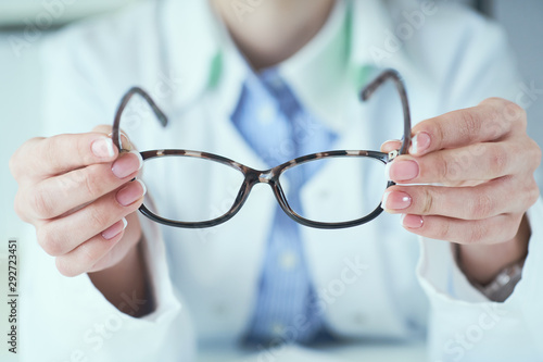 Female optician hands giving new glasses to customer for testing and trying close-up. Eye doctor with client comparing spectacles and choosing lenses in store.