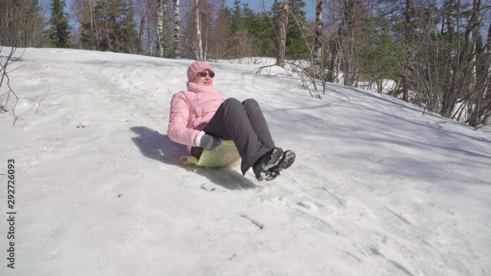 The cheerful grandmother is a senior citizen, she feels well and plays joyfully on the street. Riding from a snow slide, she smiles and laughs.