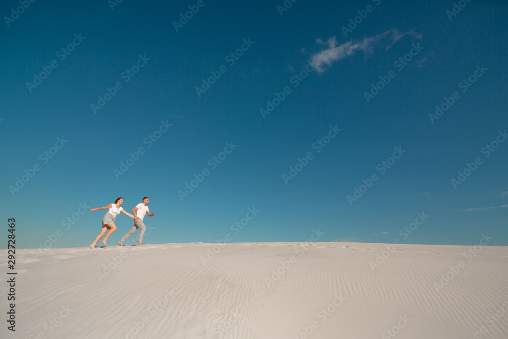 Fototapeta premium Romantic couple in love running on white sand in desert.