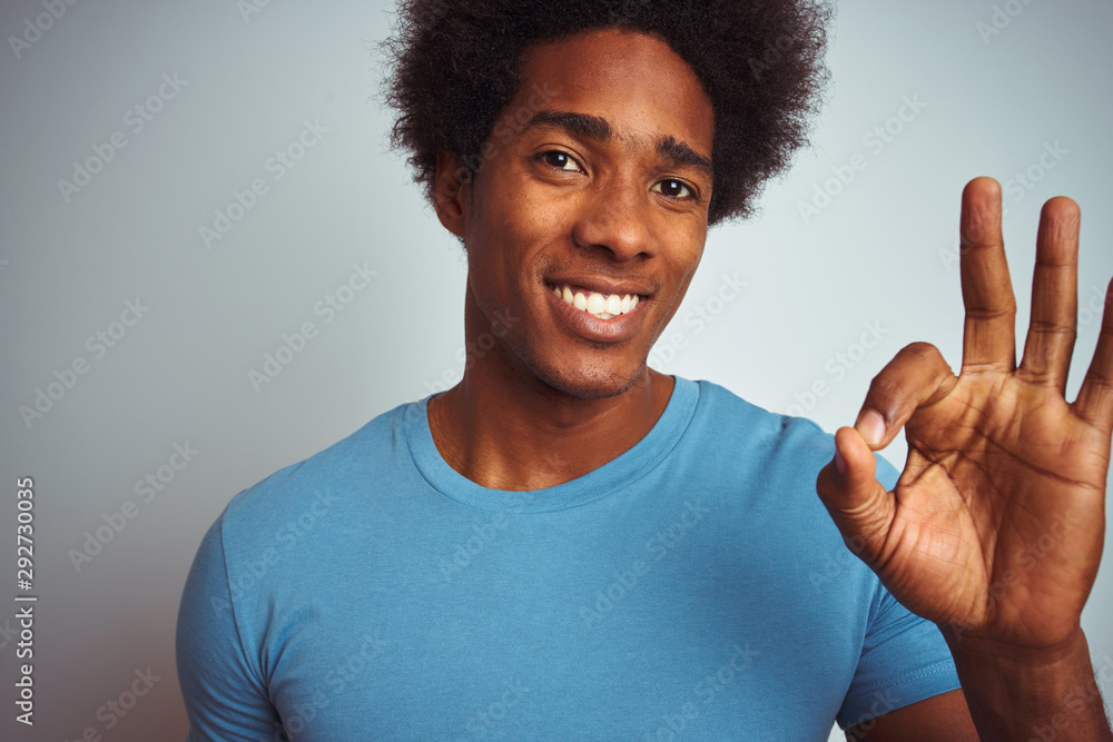 African american man with afro hair wearing blue t-shirt standing over isolated white background doing ok sign with fingers, excellent symbol African american man with afro hair wearing blue t-shirt standing over isolated white background doing ok sign with fingers, excellent symbol