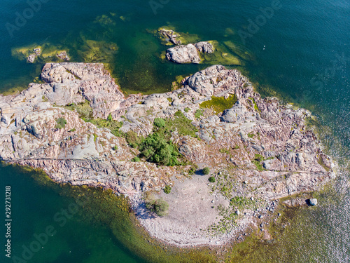 Small islet made of rocks and some trees from high altitude, calm sea and some of the seafloor visible a sunny summer day photo