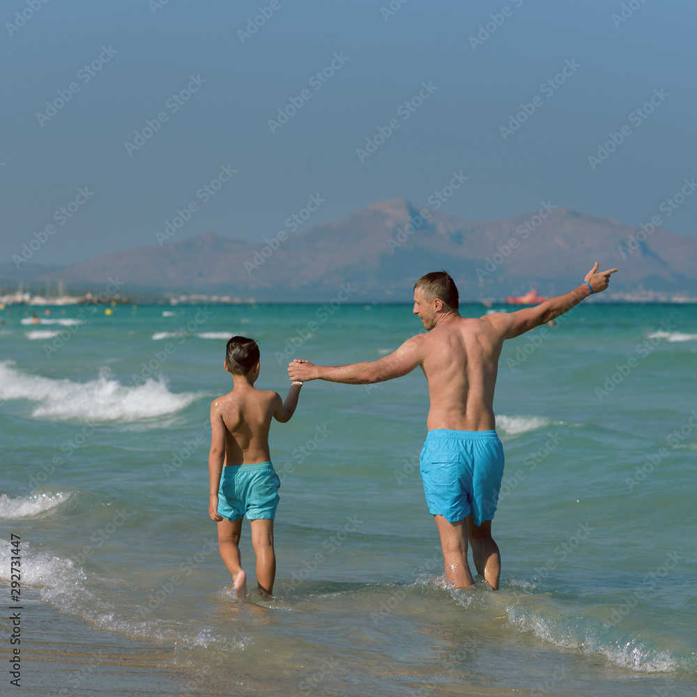Father and son enjoying their summer holidays, they are running into the sea holding hands.