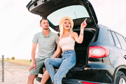Happy couple hugging at open trunk of hatchback car and pointing finger outdoors © F8  \ Suport Ukraine