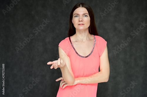 Portrait of a pretty young brunette woman with combed hair on a gray background in a pink blouse. It is in different poses. Looks straight at the camera. Slim figure.