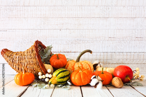 Thanksgiving cornucopia filled with autumn vegetables and pumpkins against a rustic white wood background