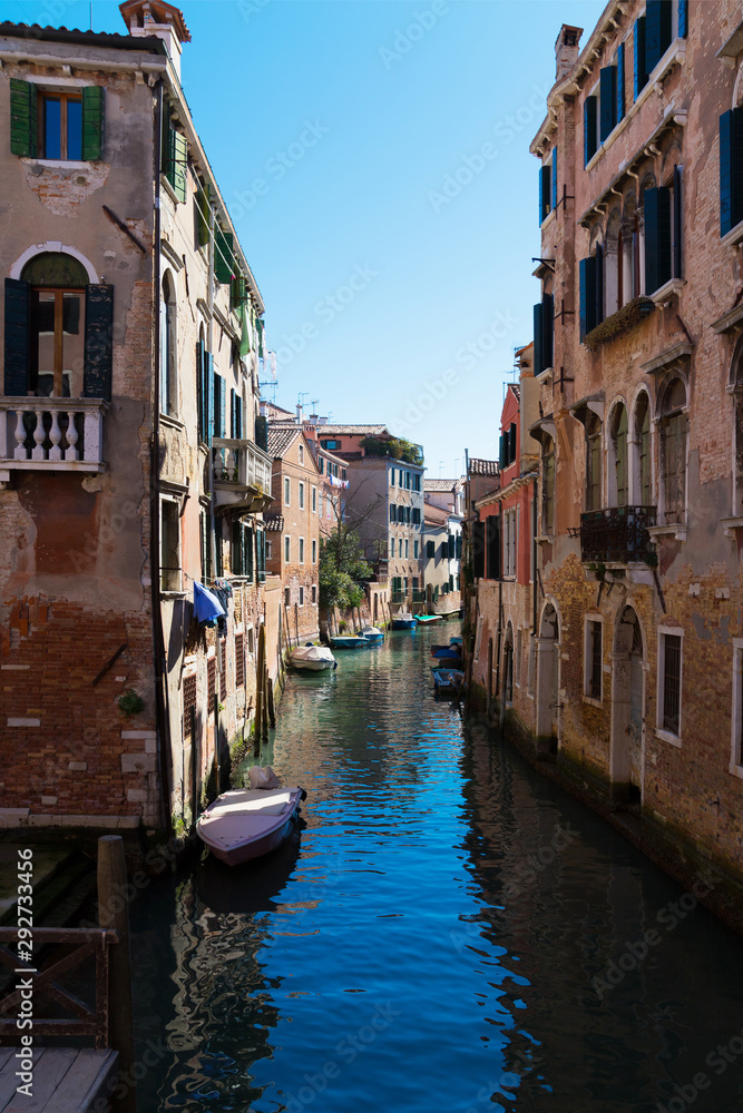 Old narrow canal with parked boats, Venice, Italy. Traditional flooded street or alley of Venice. Vertical view.