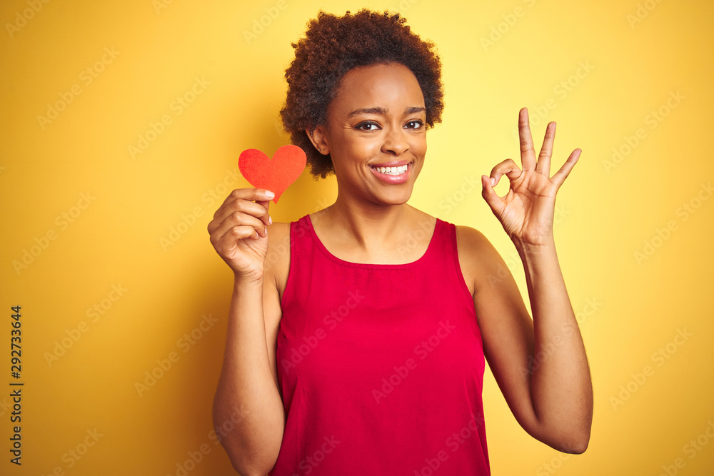 African american woman holding romantic paper hearts over yellow isolated background doing ok sign with fingers, excellent symbol